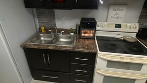 A kitchen with a double sink, a toaster, a stove, and a sign that says "Eat Cake for Breakfast".