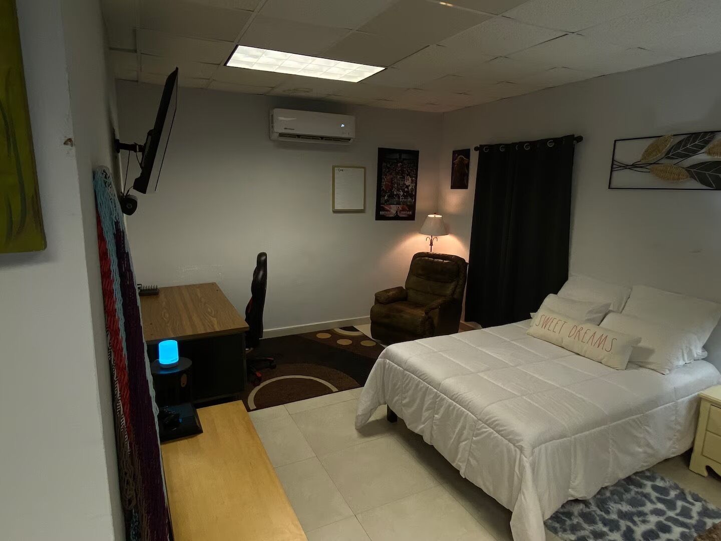 Une petite pièce, de taille modeste, comprenant un lit, un bureau, une chaise et une lampe.