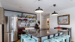 Una cocina moderna con una isla central, taburetes de bar, electrodomésticos de acero inoxidable y una variedad de utensilios y adornos de cocina.