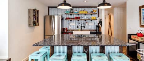 A kitchen with a central island, bar stools, and a variety of kitchen appliances and decorations.