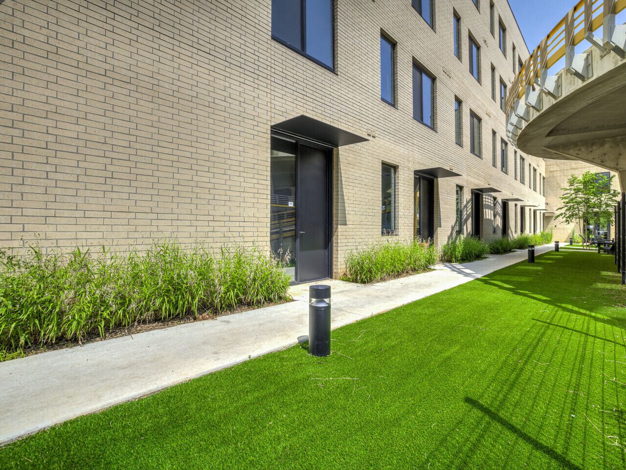Un bâtiment moderne à la façade en briques, doté d’une pelouse bien entretenue et d’un chemin menant à l’entrée.