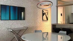 A modern dining area with a round glass table, grey chairs, a brick wall, and a hanging light fixture. - Itaim Star 2 (São Paulo)