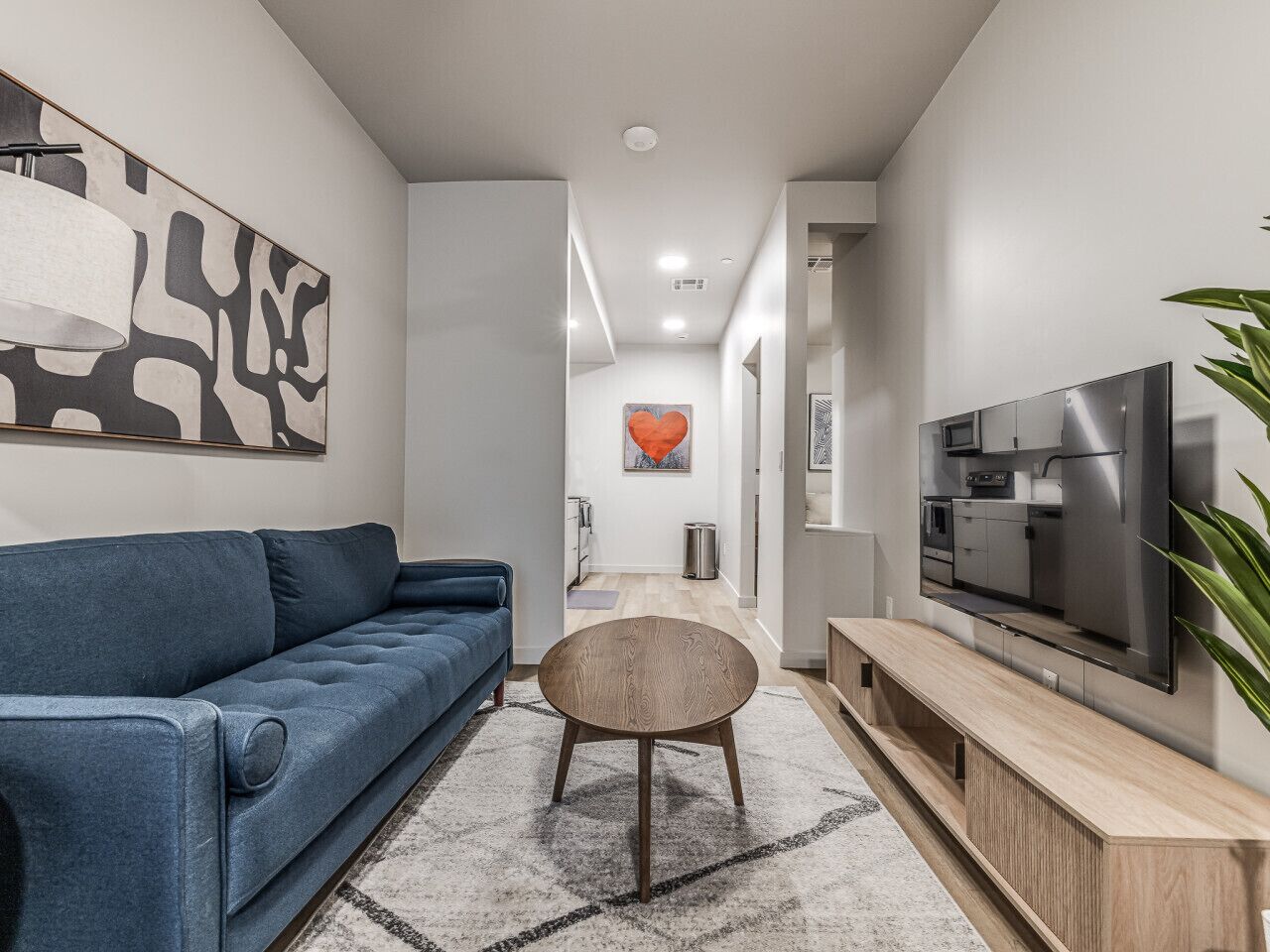Un salon moderne avec un canapé bleu, une table ronde en bois et un téléviseur posé sur un meuble en bois.