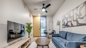A modern living room with a flat-screen TV, a blue sofa, a round coffee table, and a ceiling fan. - Midtown Luxe 1 Bed Apt (Oklahoma City)