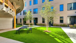A courtyard with artificial grass, two benches, and a modern building with multiple windows. - Midtown Luxe 1 Bed Apt (Oklahoma City)