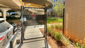A gated parking area with a concrete structure overhead, a brick building to the right, and a clear sky. - Luxury 1Bed New Build Apt (Oklahoma City)