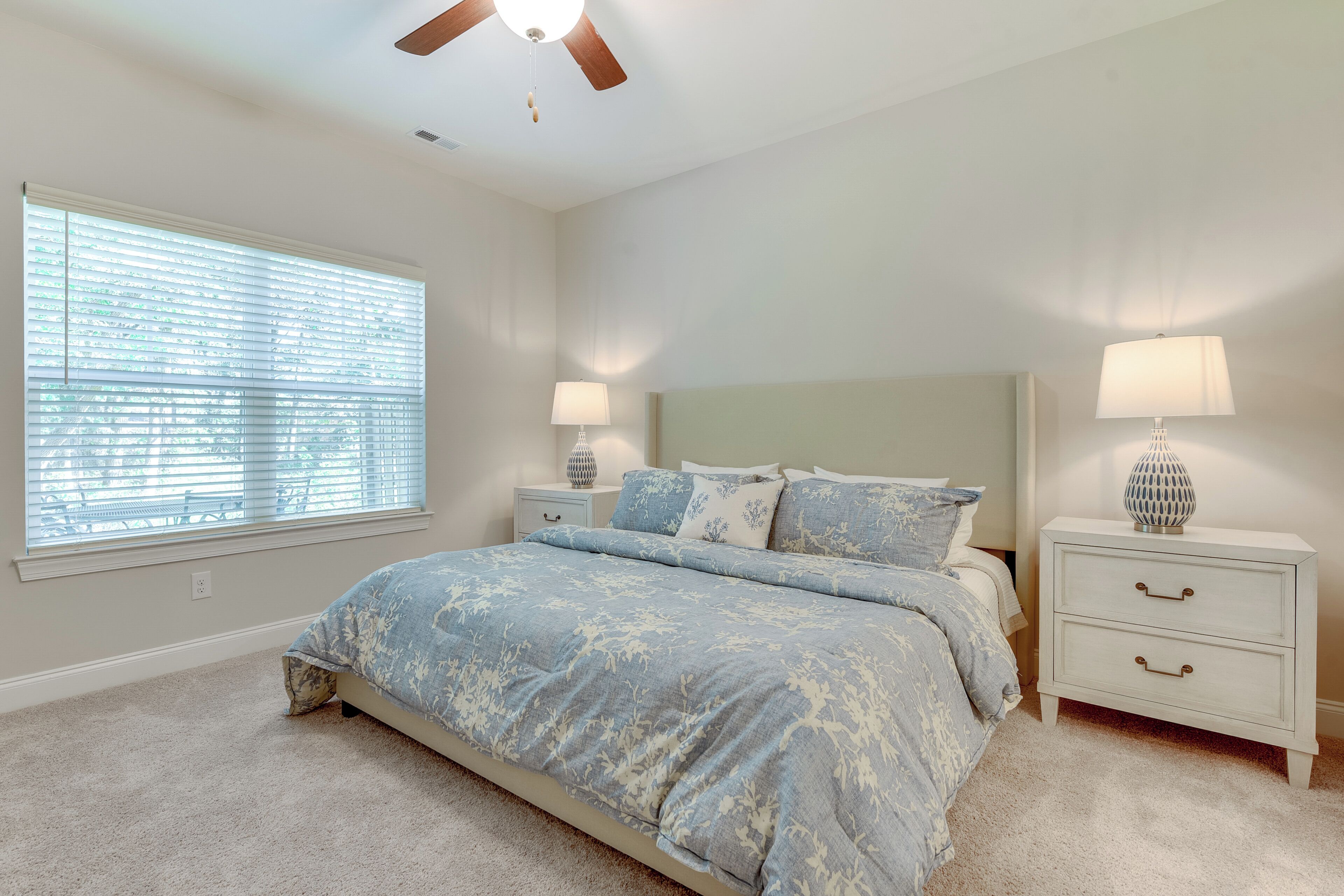 A bedroom with a bed, two nightstands, a ceiling fan, and a window with blinds.