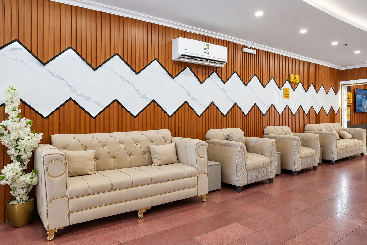 A reception area with a beige sofa, a potted plant, and a wall with a zigzag pattern.