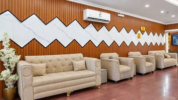 A reception area with a beige sofa, a potted plant, and a wall with a zigzag pattern.