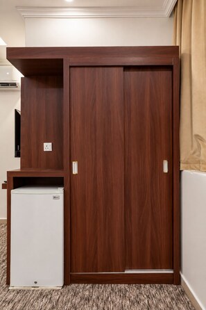 A room with a wooden wardrobe, a small white refrigerator, and a beige curtain. - MG Crown Hotel 1 (Madinah)