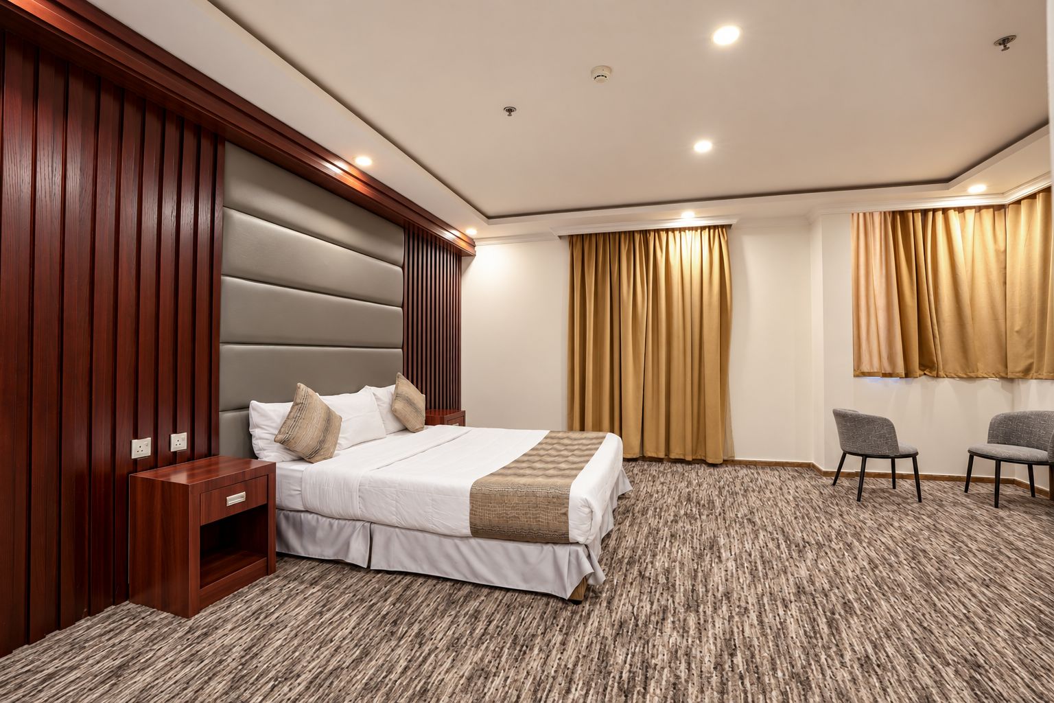 Een hotelkamer met een groot bed, een houten hoofdbord, een nachtkastje, een stoel en een vloerbedekking.