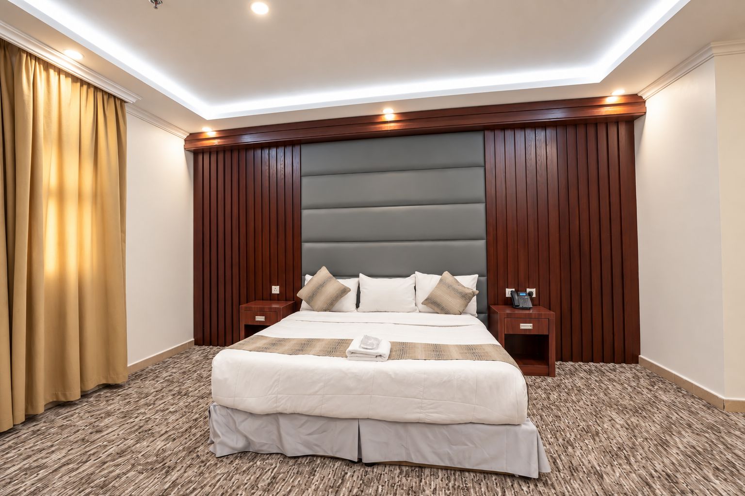 A hotel room with a large bed, wooden headboard, two bedside tables, and a telephone.