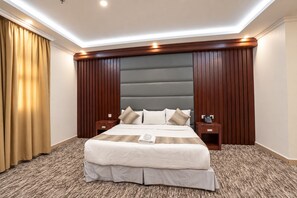 A hotel room with a large bed, wooden headboard, two bedside tables, and a telephone. - MG Crown Hotel 1 (Madinah)