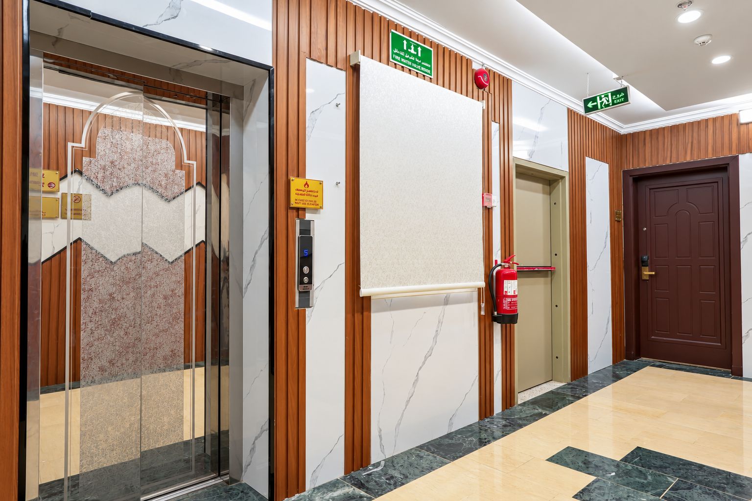 Een hotelentree met een marmeren vloer, houten lambrisering, een brandblusser en een lift.
