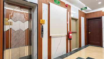 Een hotelentree met een marmeren vloer, houten lambrisering, een brandblusser en een lift.