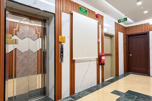 Un hall de hotel con piso de mármol, paneles de madera, un extintor y un ascensor.