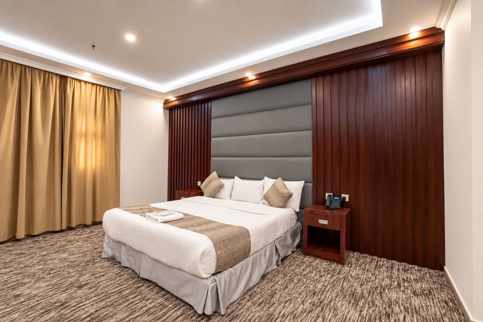 Una habitación de hotel con una cama grande, una mesita de noche con teléfono y un cabecero de madera.
