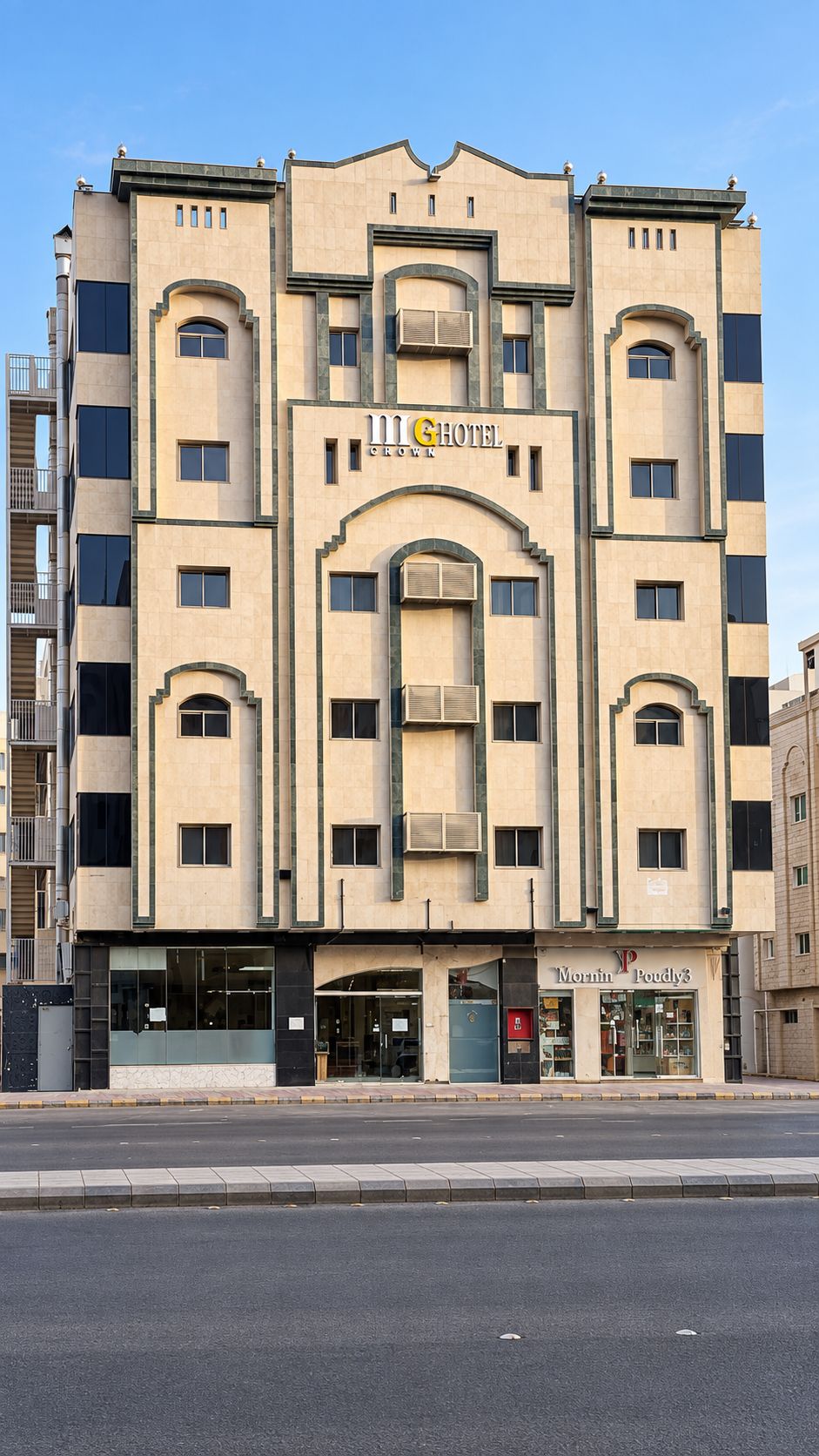 Um hotel com vários andares e um grande letreiro 'MG Hotel Crown', apresentando uma fachada simétrica com janelas em arco e uma entrada central.