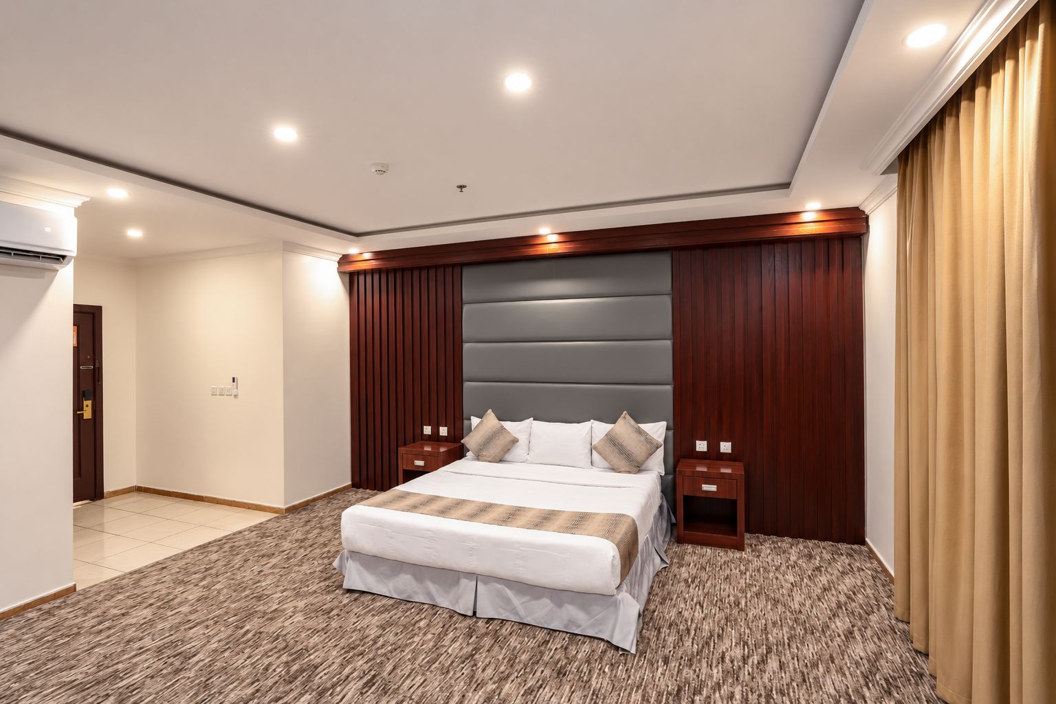 A modern hotel room with a large bed, wooden headboard, two bedside tables, and a carpeted floor.