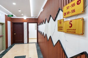 A hotel corridor with a wooden wall, a marble floor, and signs indicating the fifth floor and no smoking policy. - MG Crown Hotel 1 (Madinah)