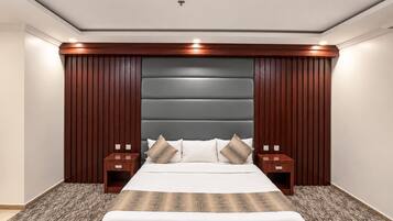 A bedroom with a large bed, wooden headboard, two bedside tables, and a carpeted floor.
