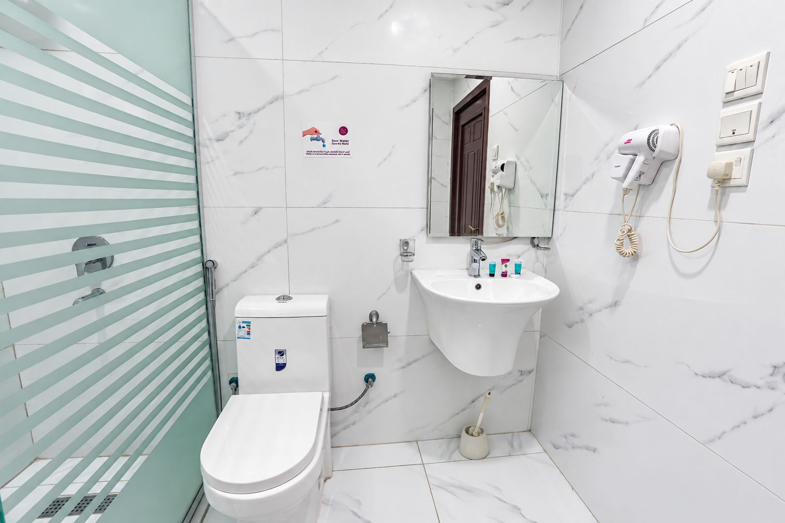 Baño con inodoro, lavabo y espejo. Hay un perchero y un secador de pelo en la pared.