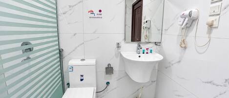 Baño con inodoro, lavabo y espejo. Hay un perchero y un secador de pelo en la pared.