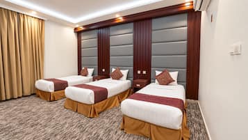 Een hotelkamer met drie bedden, elk met een bruine stoffen onderrok, een witte matras en een bedsprei met dessin. De kamer heeft een groot gestoffeerd hoofdeinde, een vloerbedekking en een raam met gordijnen.