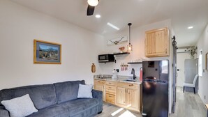 A modern living room with a grey sofa and a kitchen area featuring wooden cabinets, a stainless steel refrigerator, and a microwave. - On 90 Scenic Acres! Rural Hot Springs Retreat (Hot Springs)
