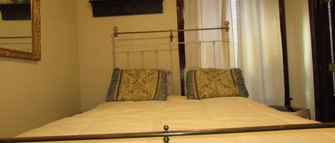 Una cama bien hecha con cabecera, dos almohadas y un espejo decorativo en la pared.