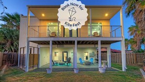 Een tweelaags huis met een balkon, een patio met buitenmeubilair en een bord waarop een vliegerfestival wordt aangekondigd.