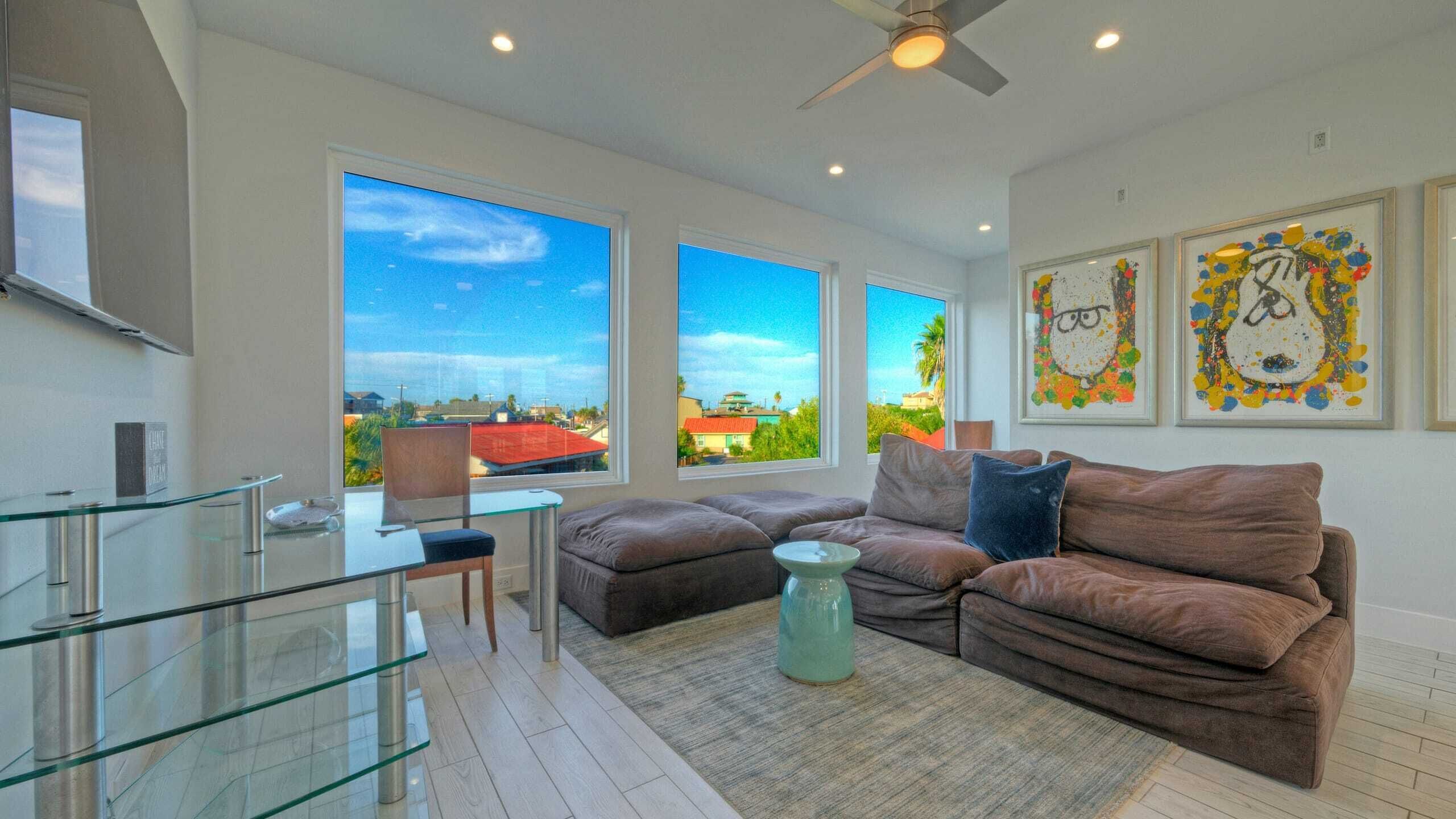 Ein modernes Wohnzimmer mit einem Glastisch, einer braunen Couch und großen Fenstern mit Blick auf die Stadt.