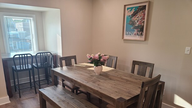 A dining room with a wooden table, six chairs, a bench, and a vase of flowers.