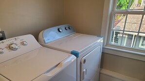 A laundry room with a front-loading washer and dryer, a window with a view of the outside, and a wooden floor.