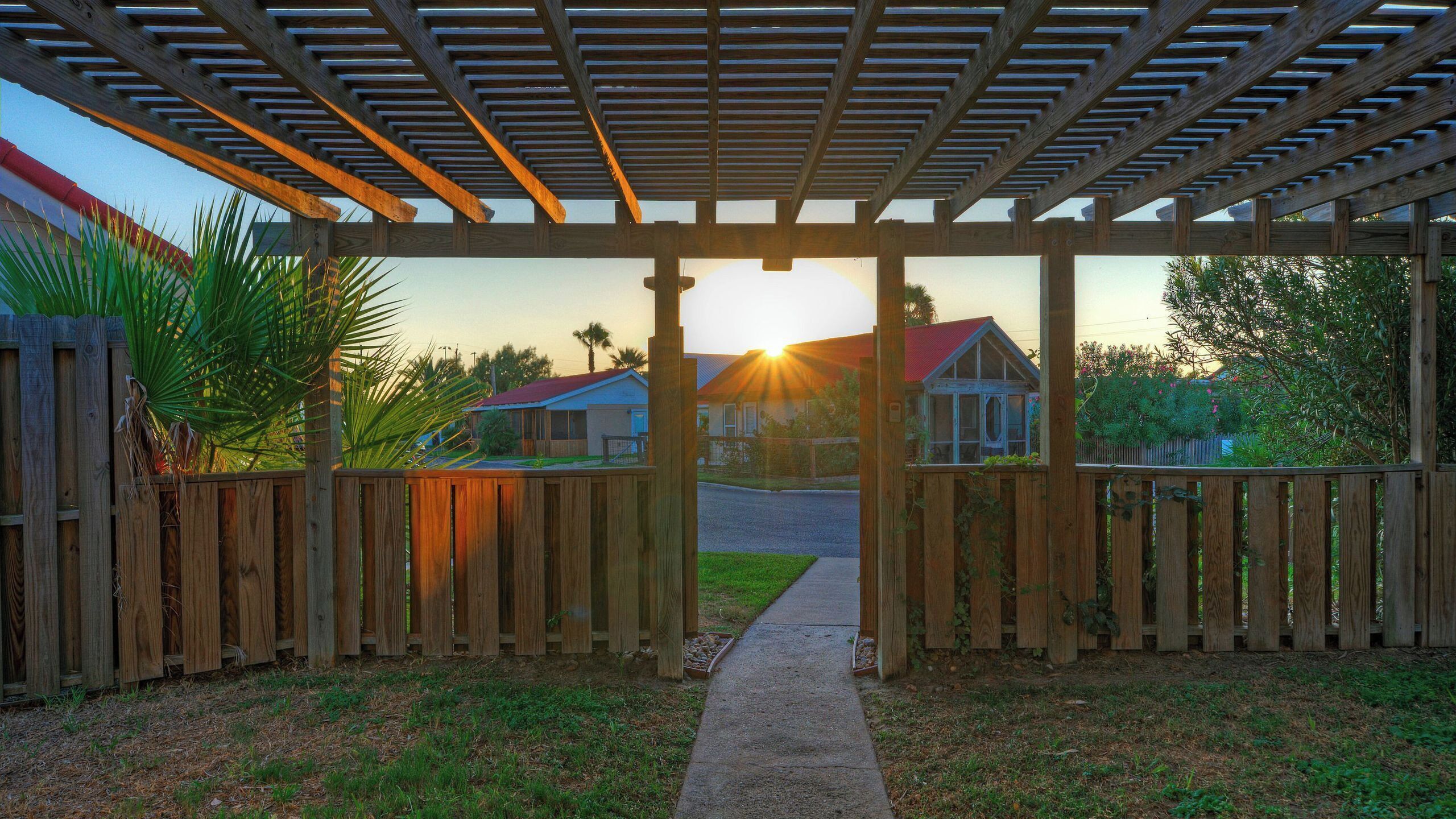 A wooden pergola structure with a pathway leading to a residential area.