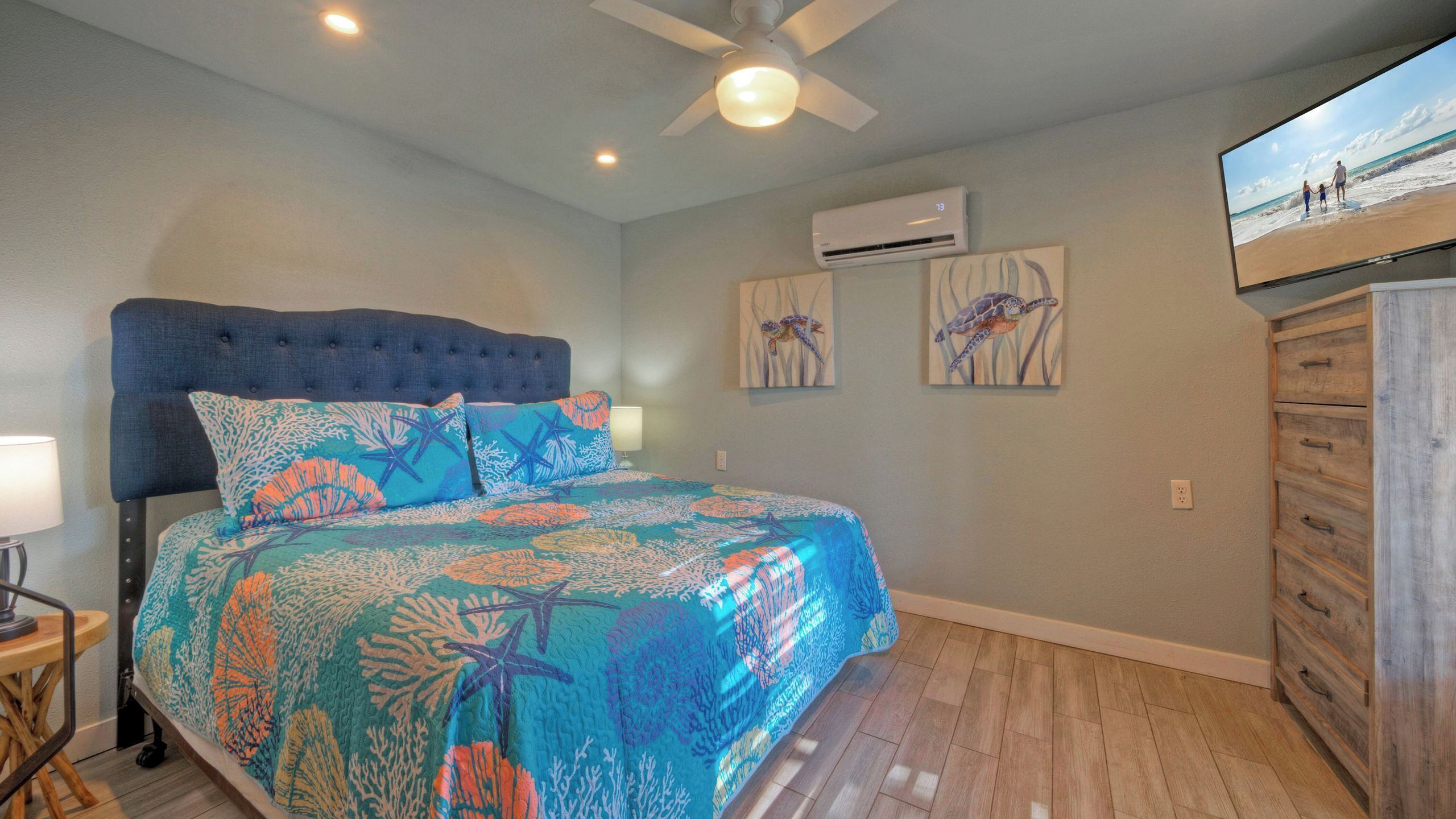 Un dormitorio con cama, ventilador de techo, aire acondicionado y televisor en la pared.