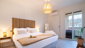 Una cama bien hecha con sábanas blancas, cabecera de madera y mesita de noche con lámpara.
