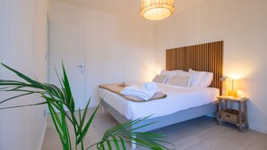 Una cama bien hecha con cabecera de madera, una lámpara de noche y una mesita de noche de madera con una cesta.