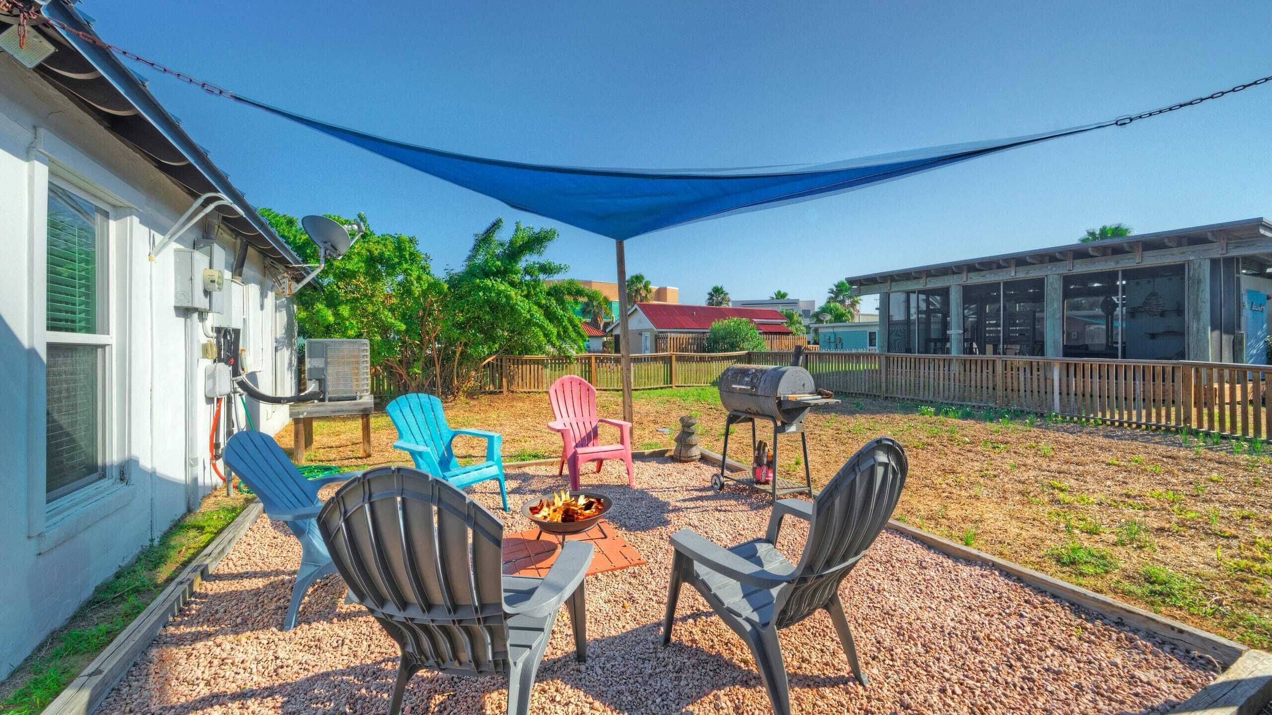 An outdoor patio with a barbecue grill, two Adirondack chairs, and a fire pit.