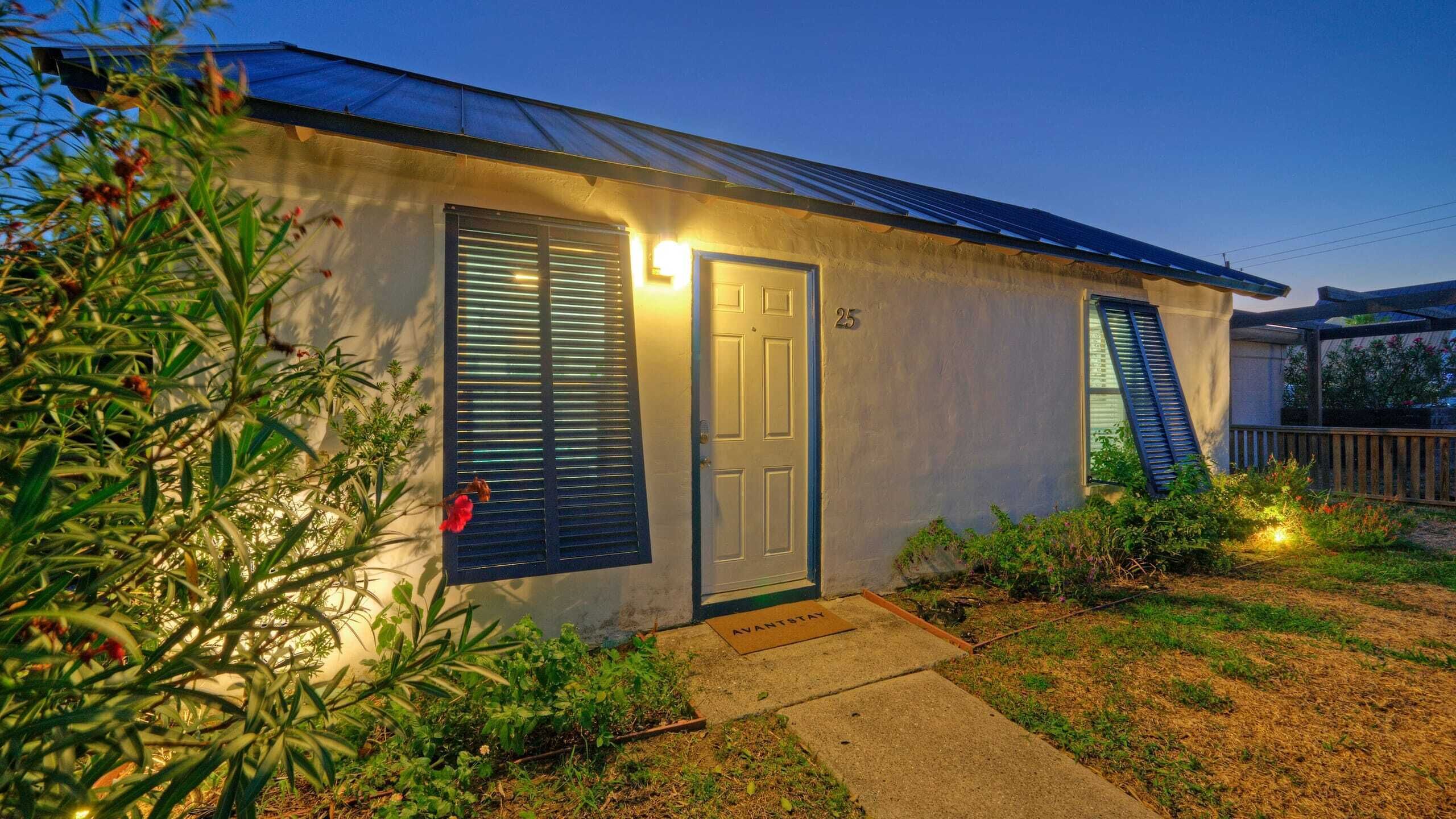 A single-story house with a dark door and shutters, a small front yard, and a number '25' on the wall.