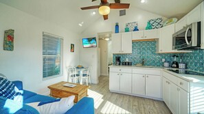 A compact kitchen with white cabinets, a microwave, and a coffee maker. There is a dining area with a table and chairs, and a ceiling fan. - Walk to Alister St Near Dining, King Suite, w/ Private Yard & Fire Pit Casa Santori by Avantstay (Port Aransas)