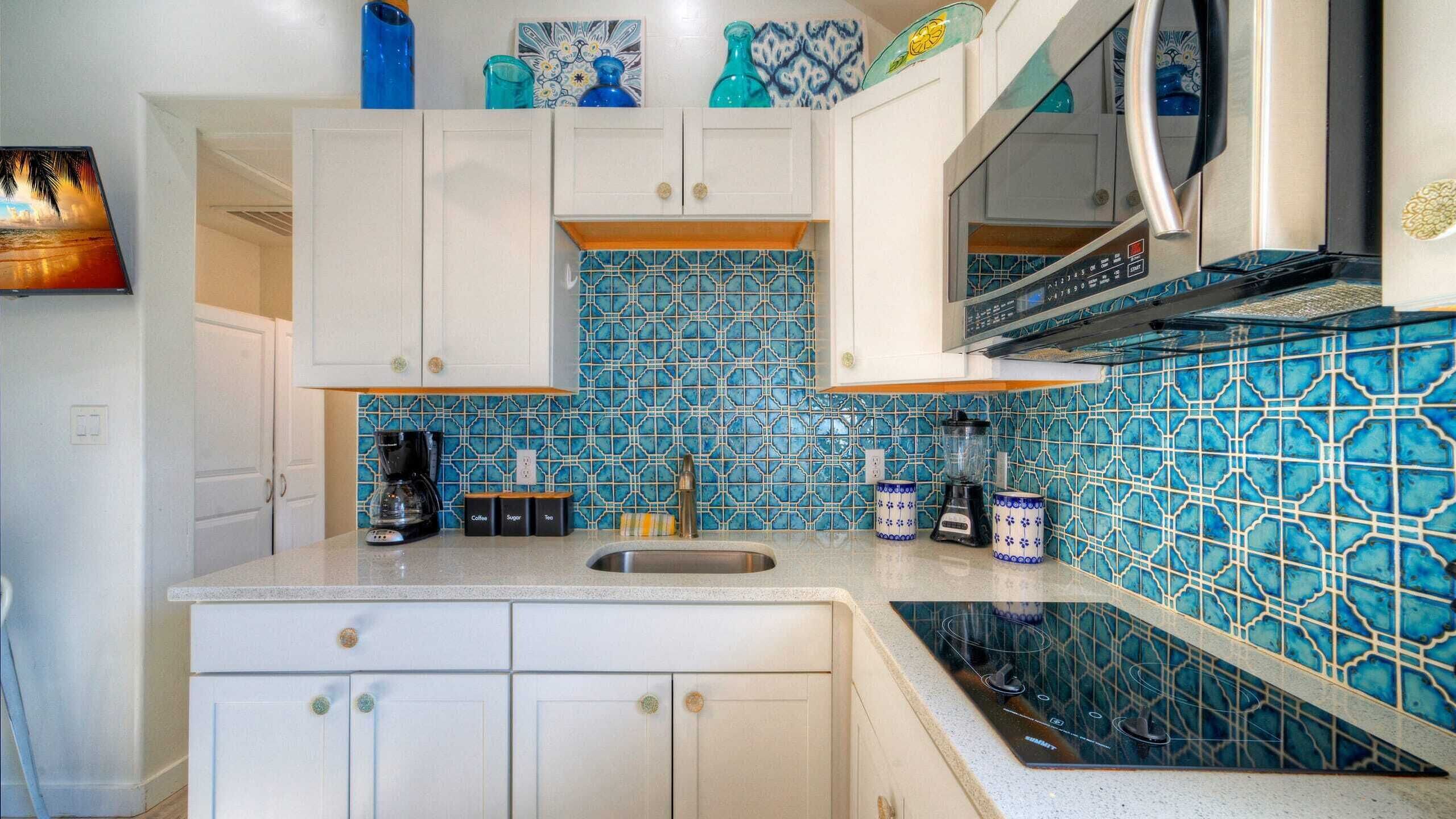 A kitchen with white cabinets, a blue tiled backsplash, a coffee maker, a blender, and a microwave.