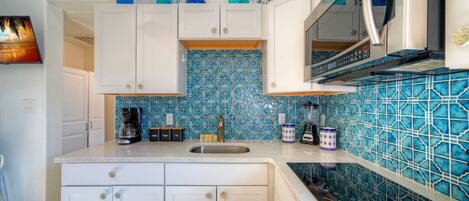 A kitchen with white cabinets, a blue tiled backsplash, a coffee maker, a blender, and a microwave.