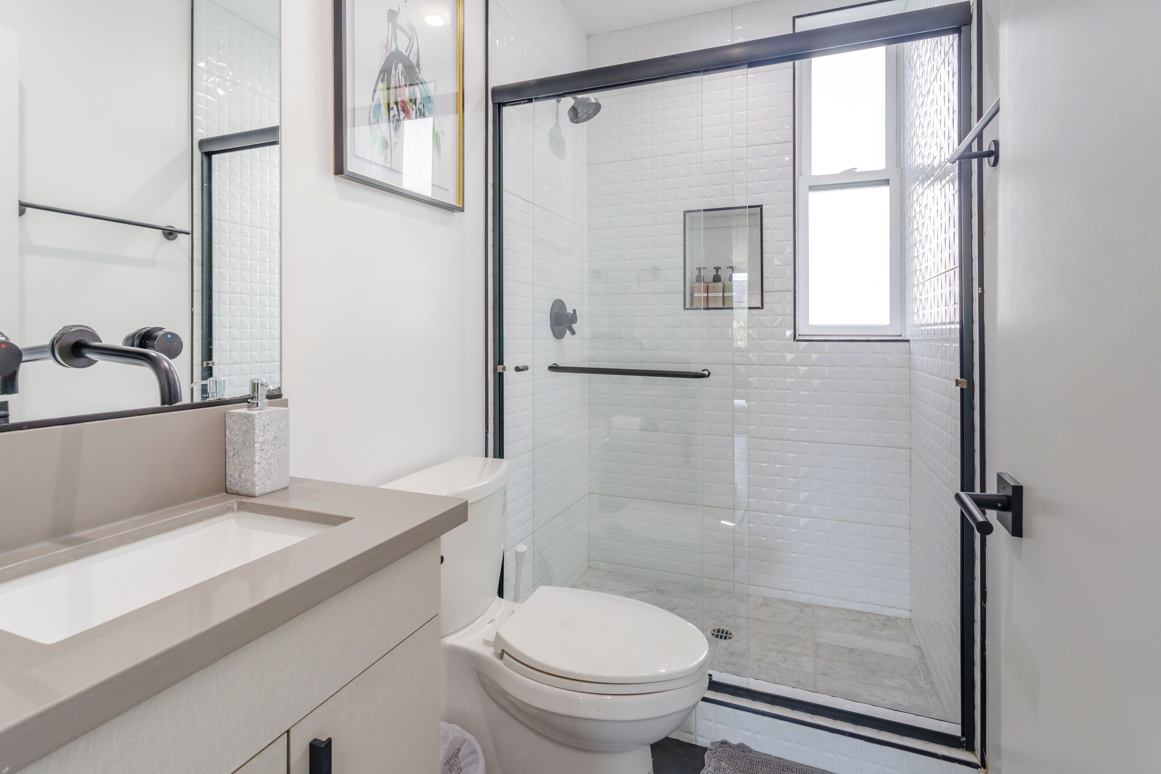 Een moderne badkamer met een douche in een glazen cabine, een wit toilet en een beigekleurde wastafelmeubel.