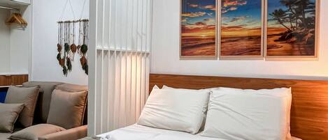 A hotel room with a bed, a sofa, a wall-mounted artwork, and a hanging macrame decoration.