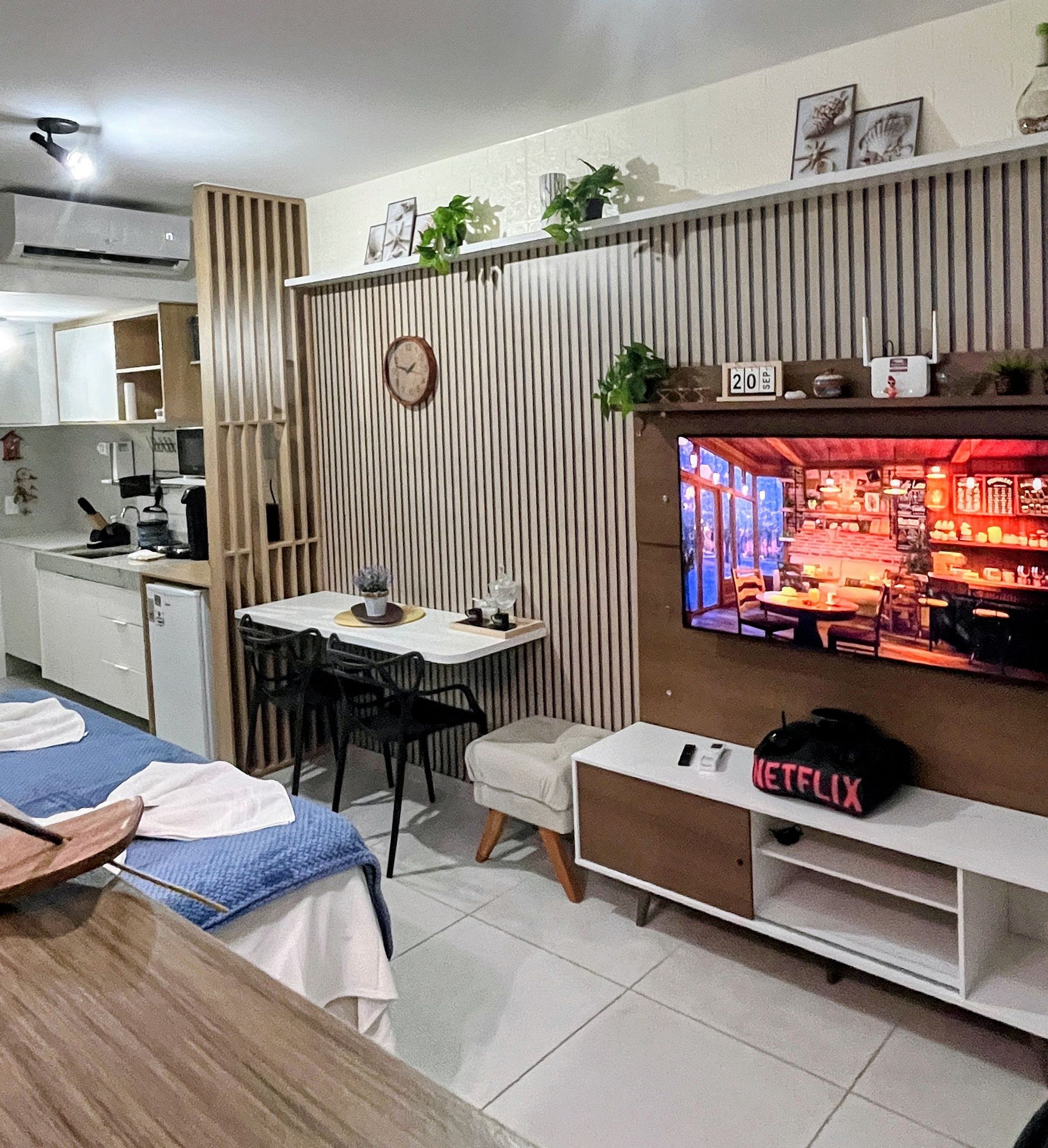 Uma sala de estar moderna com área de jantar, TV fixada na parede e pequena cozinha compacta.