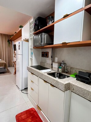 Una cocina compacta con microondas integrado, un lavamanos y una encimera con tostadora.