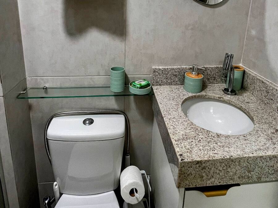 Baño con inodoro, lavabo, espejo, toallero y estante de vidrio con artículos de aseo.