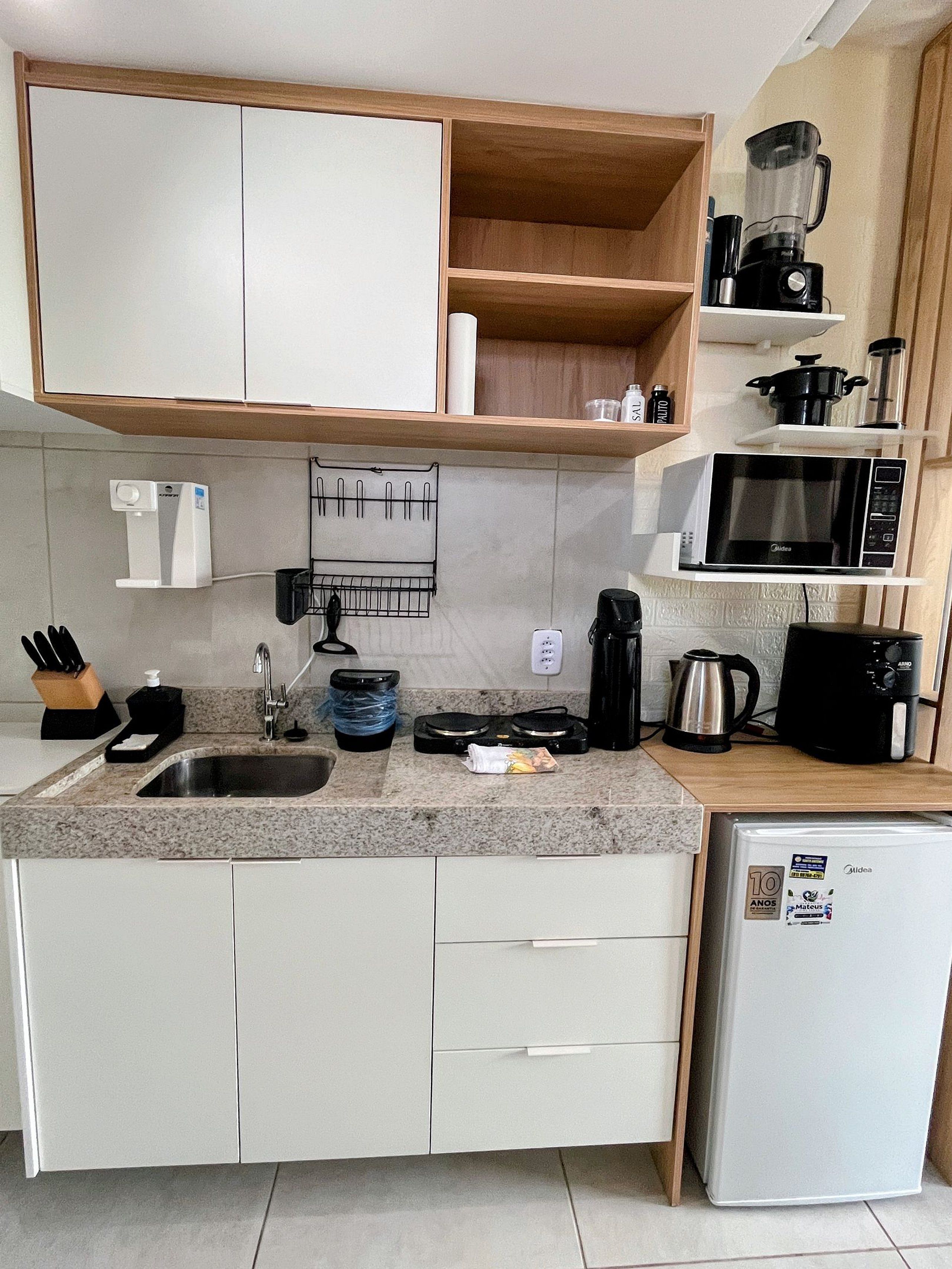 Cozinha compacta com micro-ondas embutido, máquina de café e geladeira.
