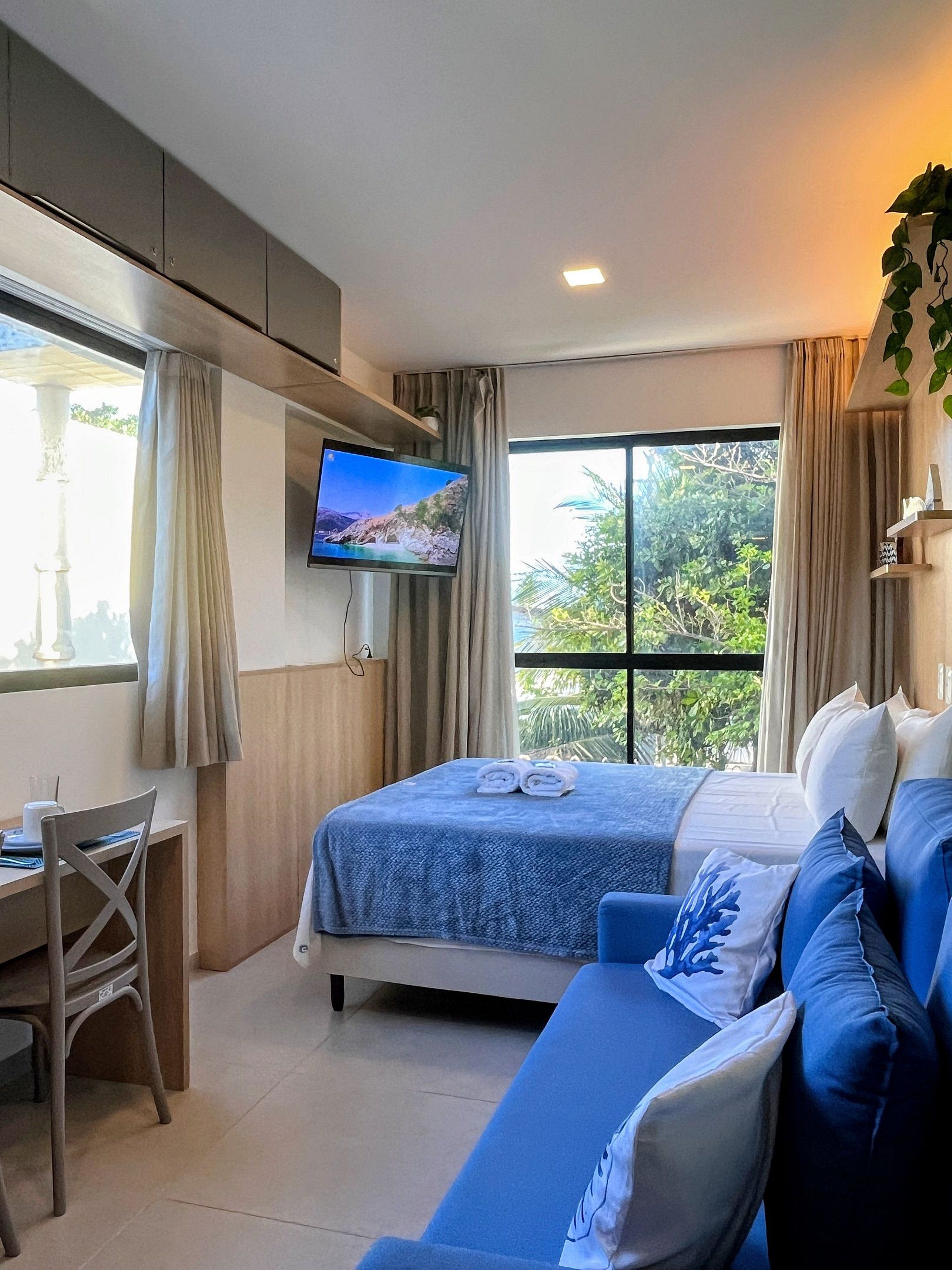 Een hotelkamer met een bed, bureau, televisie en een groot raam.